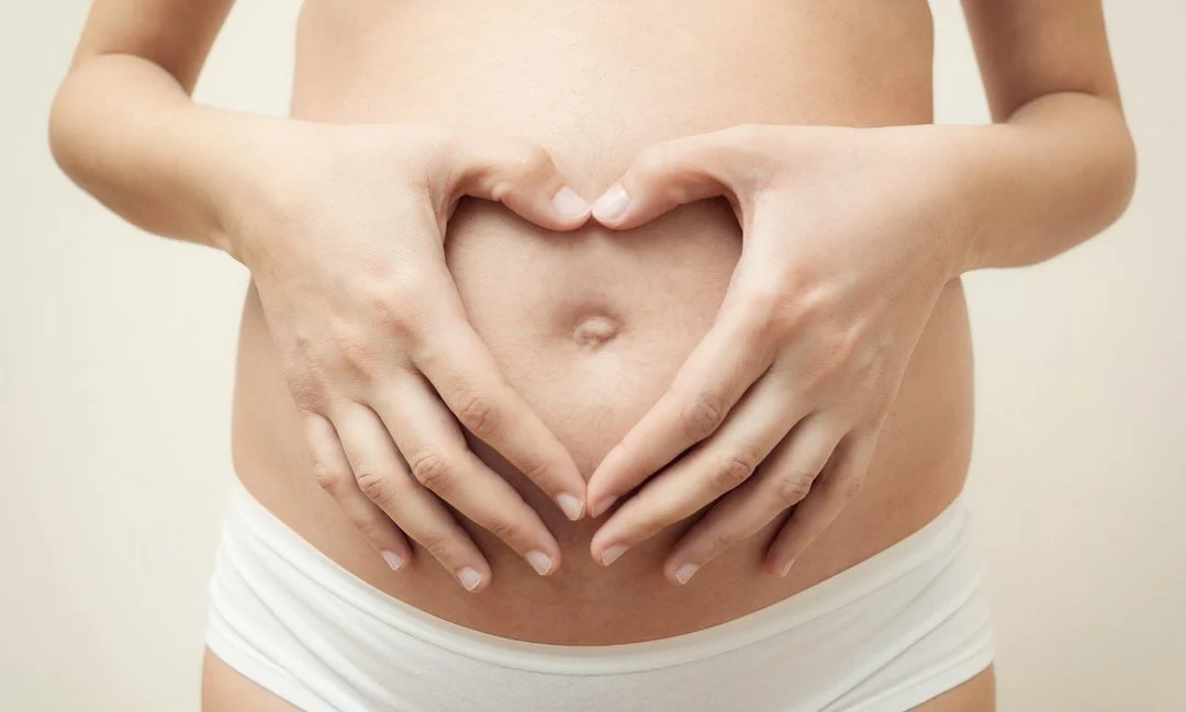 Pregnant woman making a love heart shape with her fingers on her belly